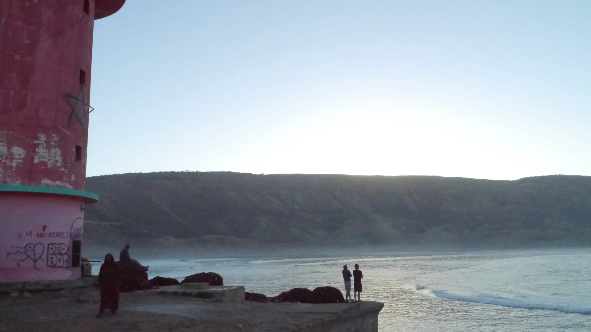 La baie d'Imsouane au lever du soleil — surfeurs alignés sur le long mur droit de la Cathédrale, l'une des plus longues vagues d'Afrique du Nord