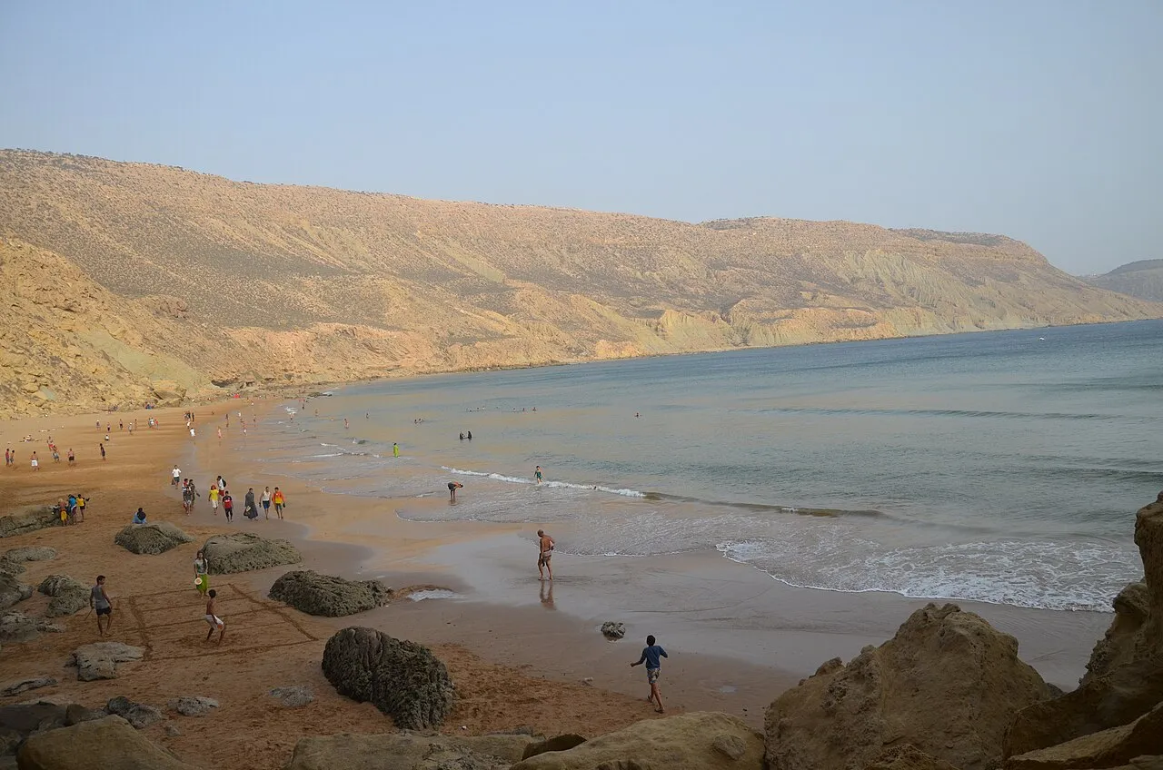 La plage sud d'Imsouane vue depuis les rochers — la baie s'ouvre vers le nord avec les collines en arrière-plan