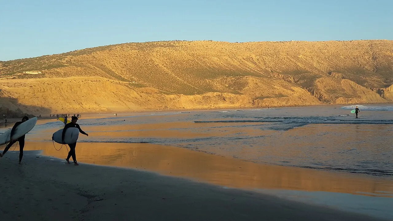 Coucher de soleil à Imsouane — surfeurs marchant sur le sable mouillé reflétant la lumière chaude