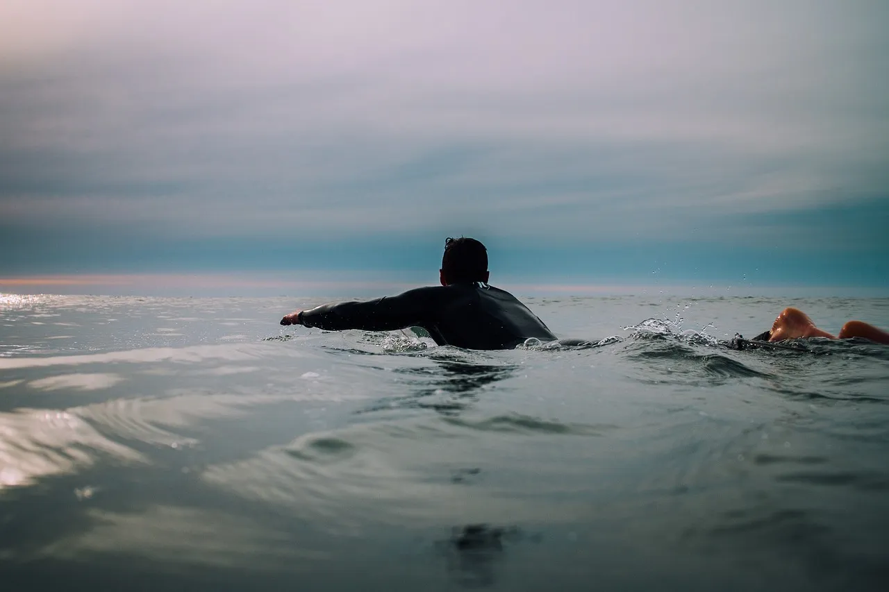 Surfeur en combinaison ramant vers le lineup — le profil de client cible du Radisson Blu, positionnement Surf Village