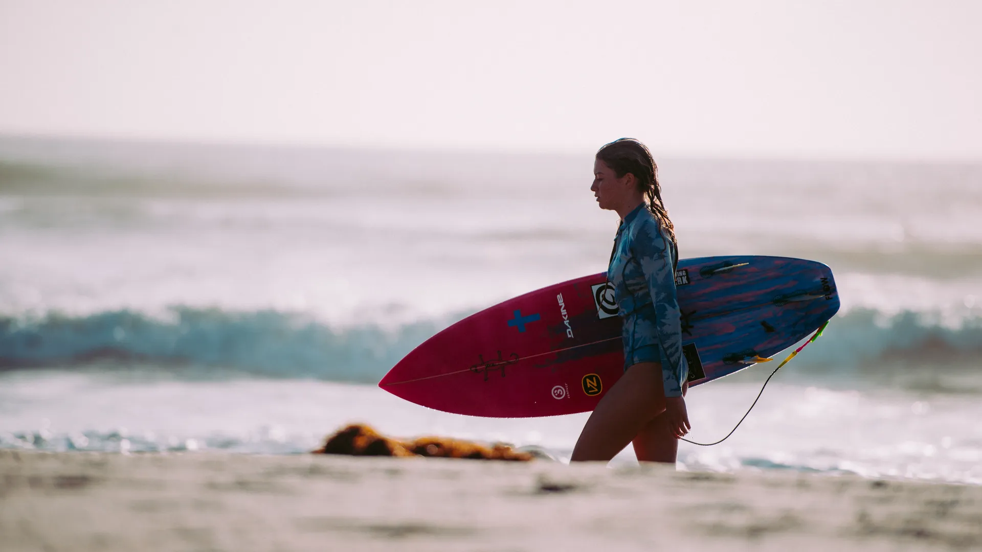 Surfeur marchant avec sa planche sur le sable — image qui résume le positionnement Surf Village du Radisson Blu Taghazout Bay