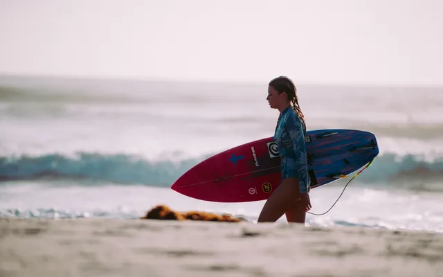 Surfeur marchant avec sa planche sur le sable — image qui résume le positionnement Surf Village du Radisson Blu Taghazout Bay